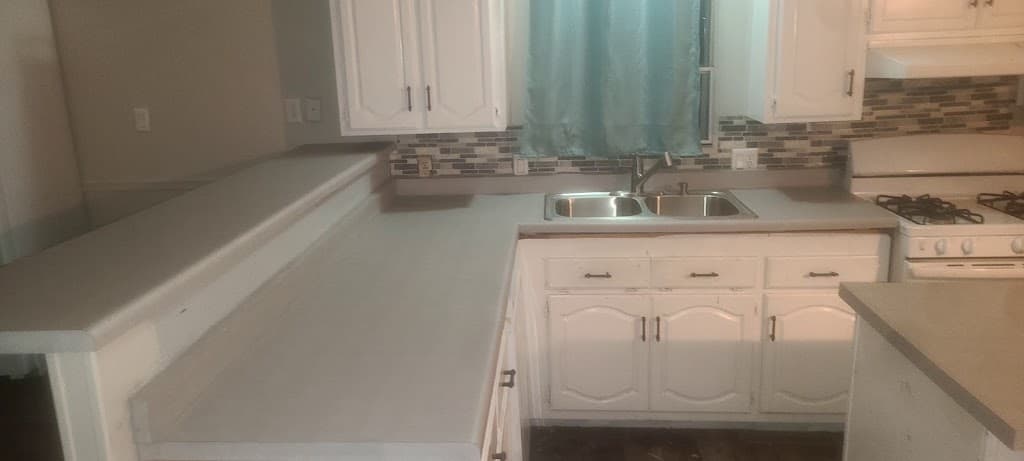 Finished kitchen with grey countertop, white cabinets, and tile backsplash